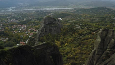 Aerial-view-flying-between-sandstone-pillars-revealing-a-person-sitting-on-a-cliff-in-Meteora,-Greece---pull-back,-drone-shot