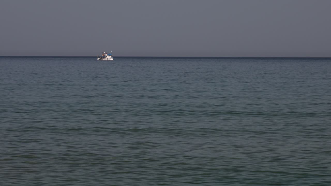 Distant ship moving slowly on calm sea under cloudy evening light