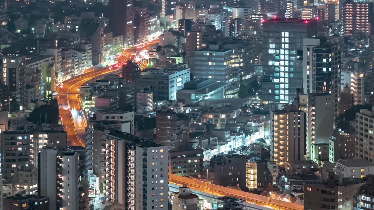 Night timelapse of traffic on a highway in the futuristic city of Tokyo. Aerial telephoto shot, zoom in.