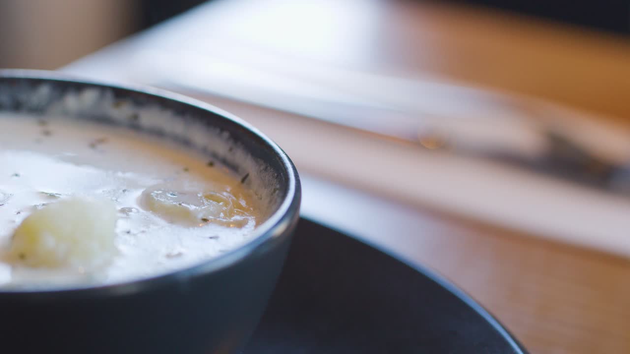 Close-up sequence of hot Cullen skink soup in a rustic bowl, with a spoon lifting creamy potato chunks. Soft natural lighting, shallow depth of field, cozy indoor setting