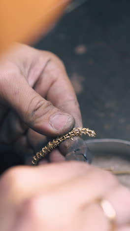 cu: professional jeweler cuts small parts from beautiful gold chain with pliers over metal box on wooden table close view