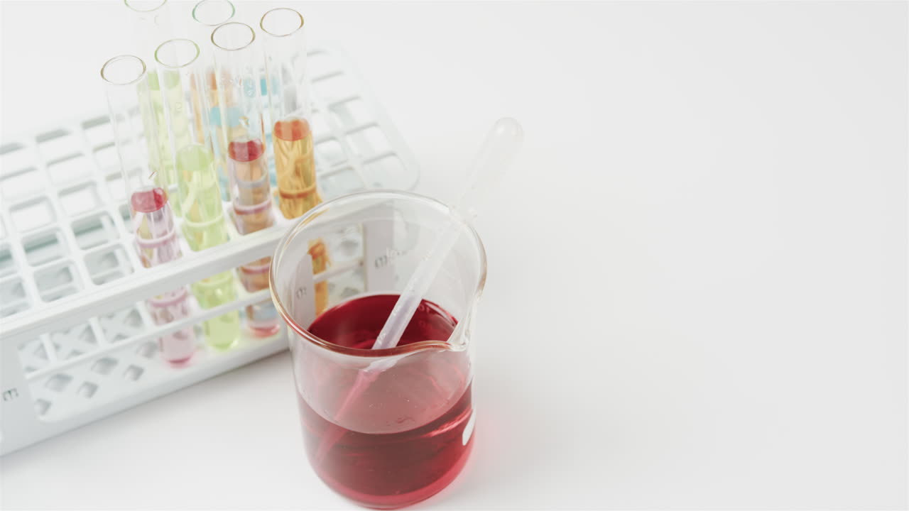 컬러 액체는 백색 배경에 시험 튜브가 서서히 움직이는 컵에 담겨 있습니다.