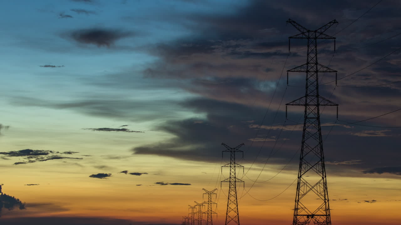 Power pylons towers strung to the horizon during cinematic colourful blue orange sunset with slow moving moody clouds