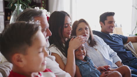 Familia-Hispana-De-Tres-Generaciones-Sentada-En-El-Sofá-Viendo-La-Televisión-Juntos,-De-Cerca