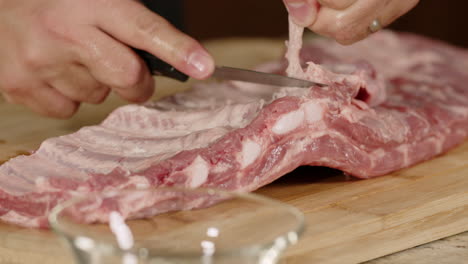 man cleans fat from raw bbq pork ribs with knife before cooking