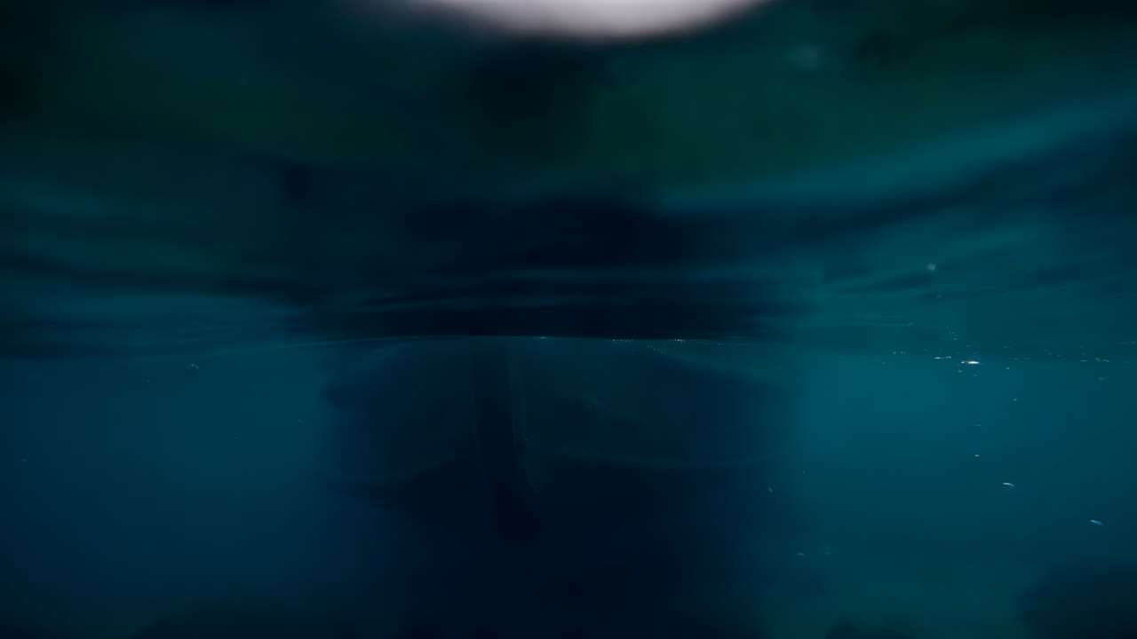 Moving hull churning beneath surface during boat passage lifting bubble columns and sunlight shafts