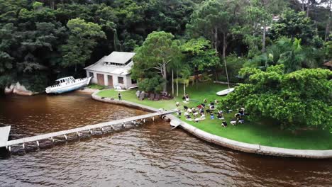 toma de órbita aérea que muestra a un grupo de turistas practicando ejercicios de yoga al aire libre en el jardín de un apartamento de vacaciones frente al océano