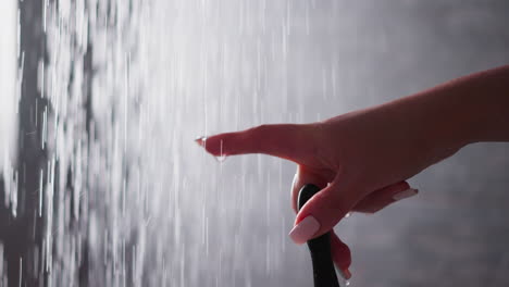 woman tries shower water by finger in bathroom closeup. lady holds razor under falling down water sprays to wash in bathroom. relaxation in washroom