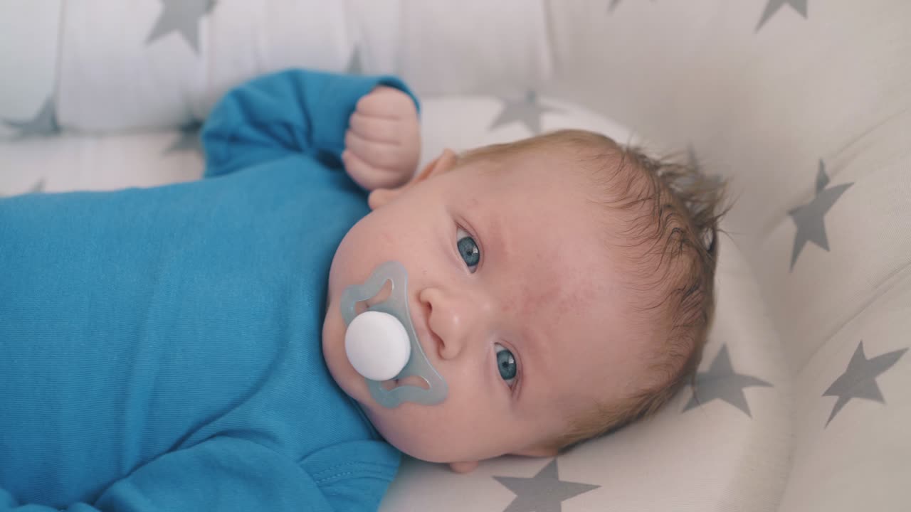 rocking lovely little kid sucking dummy in cocoon in crib