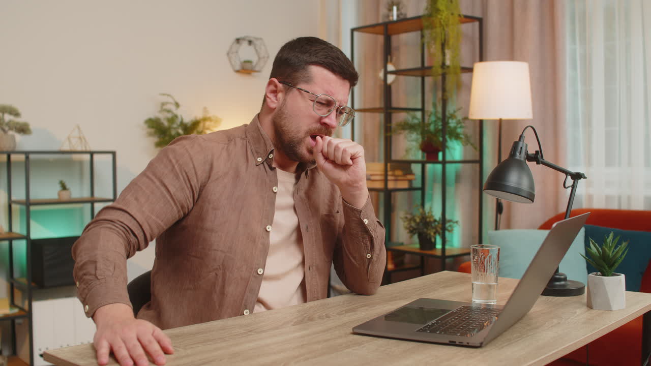 hombre enfermo freelance sintiéndose mal sufriendo de dolor de garganta toca el pecho mientras tos en casa