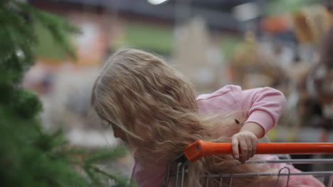 una niña en un carrito de comestibles mira un árbol de navidad en cámara lenta.