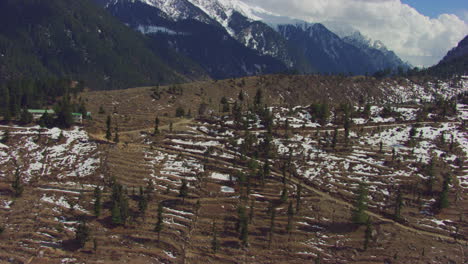 A-film-look-cinematic-aerial-camera-pan-from-Pine-forest-at-snow-mountain-to-a-house,-top-of-the-hill