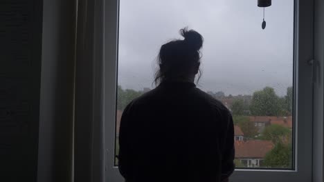 a young man in total desperation, shot from the back, in front of a rainy window