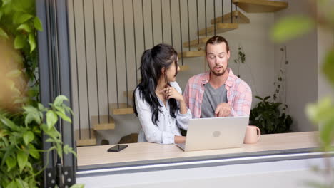 Diverse-couple-sitting,-talking,-looking-at-laptop-at-home,-copy-space