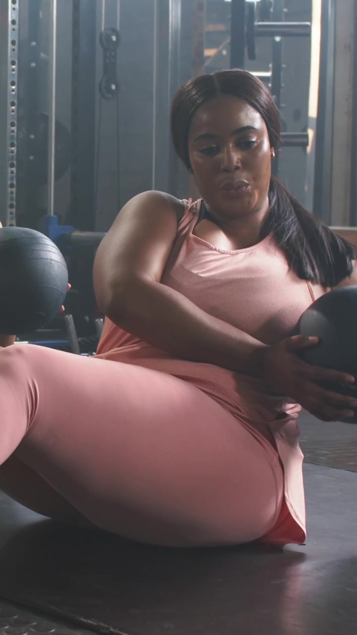 Video verticale: Torsioni su tappetino da palestra dopo un passaggio, donna in rosa che passa una palla medica nera per il core