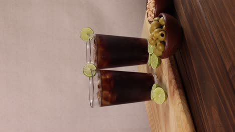piscola chilena bebida cóctel típico de verano de vidrio chileno con tabla de madera de hielo y limones en un fondo brillante con enfoque selectivo, video vertical