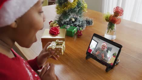 Afroamerikanische-Frau-Mit-Weihnachtsmütze-Nutzt-Tablet-Für-Weihnachtsvideoanruf,-Mit-Mann-Auf-Dem-Bildschirm