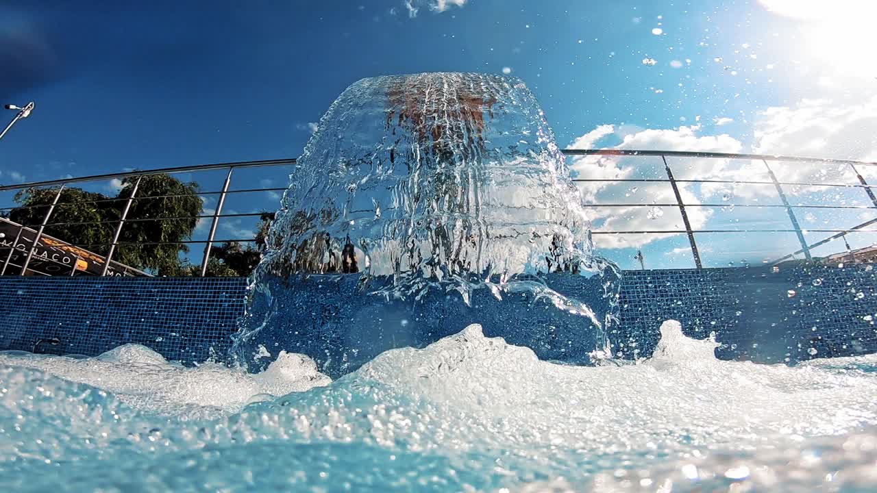 Clear water falling into the pool. Waterfall over the pool making air bubbles on water surface outdoors in sunny day. Close-up.