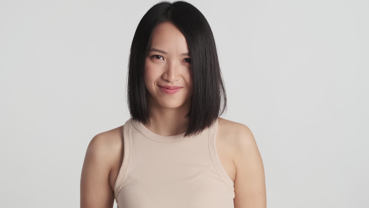 아시아 여성이 카메라 앞에서 고개를 끄덕이고 미소 짓고 있습니다.