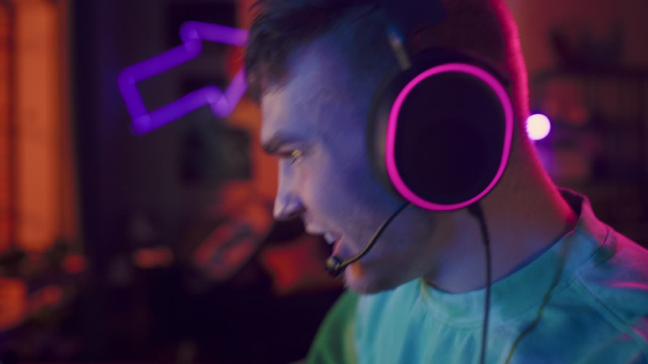juegos en casa: gamer jugando videojuegos en línea en la computadora. retrato en primer plano de un hombre exitoso con auriculares disfrutando del tiempo libre, celebrando la victoria en la ronda. juegos cibernéticos elegante sala de neón retro.