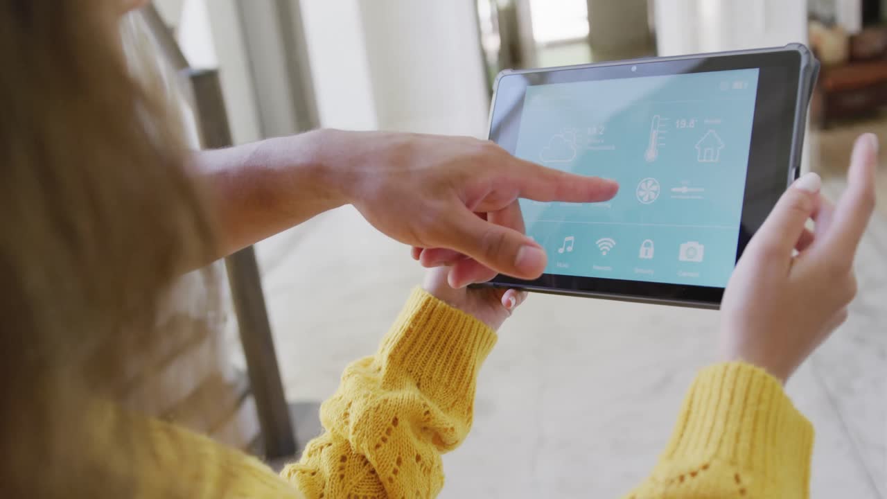 pareja biracial que pasa tiempo en casa usando una tableta con interfaz de hogar inteligente