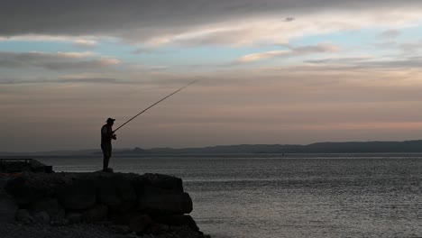 anciano pescando desde un muelle de roca en el lago durante el hermoso atardecer de verano