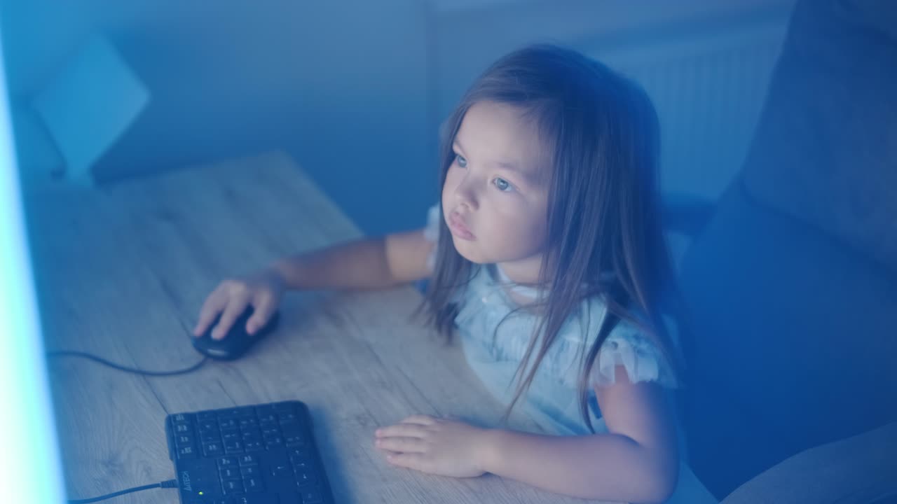 어린 소녀가 컴퓨터 앞에 앉아서 강한 감정을 표시합니다. 이 장면은 편안한 실내 환경에서 펼쳐지는 매력적인 순간 동안 그녀의 표현적 반응을 포착합니다.