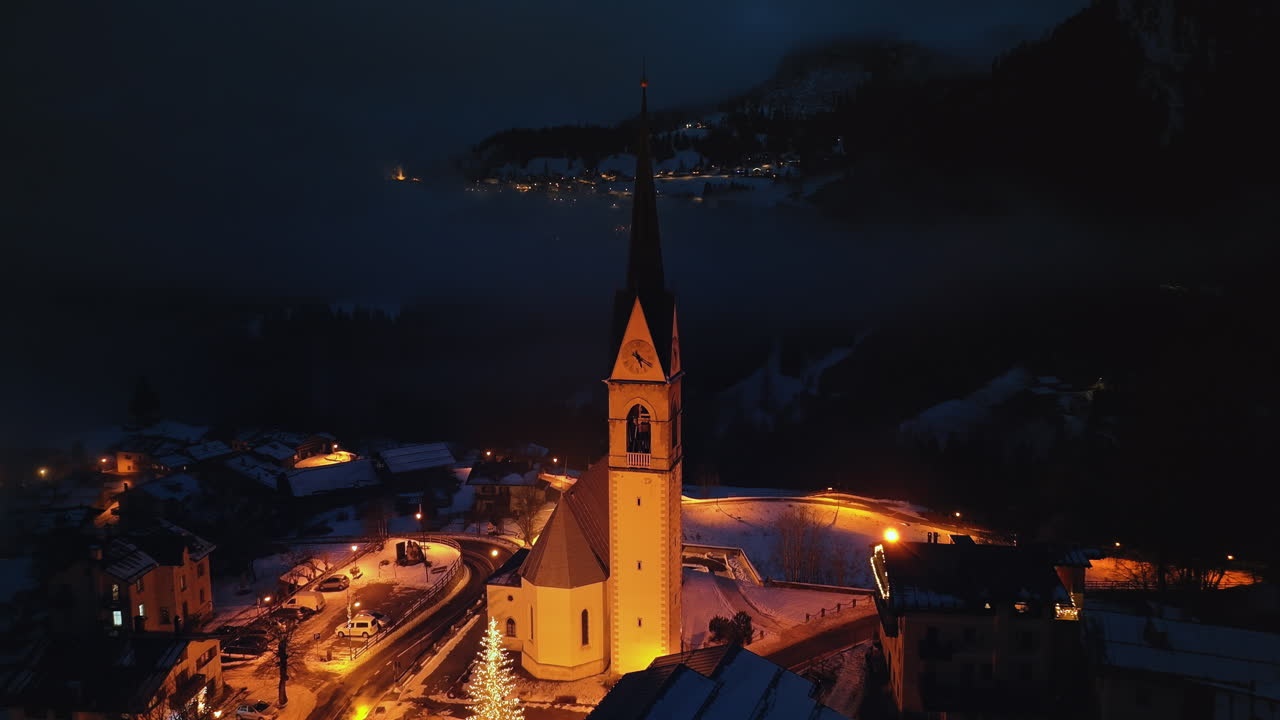 Aerial drone view of the San Lorenzo Church illuminated at night in the Selva di Cadore comune in Dolomites, Italy