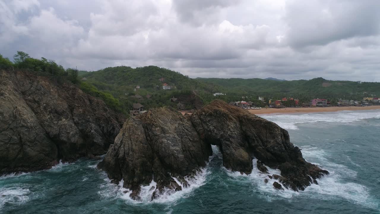 Ripresa aerea in picchiata di una grande formazione rocciosa con una porta al centro, spiaggia di Zipolite, Oaxaca