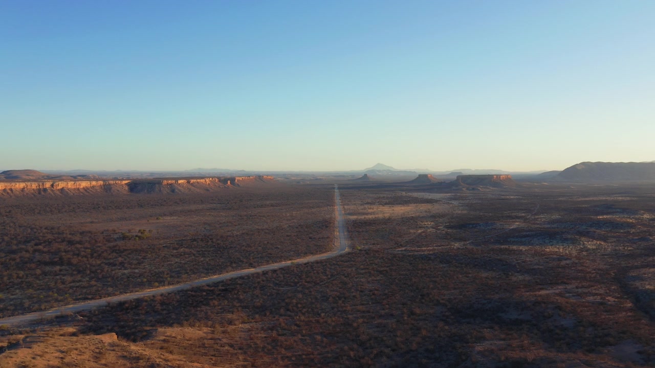 Vista panorámica con dron del Valle de Uganda y las Terrazas de Ugab cerca de Fingerklippe al atardecer, mostrando una larga carretera recta que atraviesa formaciones geológicas dramáticas