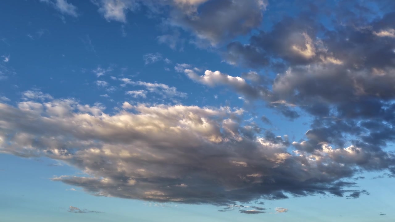 4K UHD timelapse: prominent morning cloud formations dominate the frame against a blue backdrop. Dynamic atmospheric transition captures crisp dawn sunlight illuminating the drifting weather layers.
