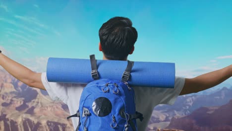 close up back view of a male hiker with mountaineering backpack spreading arms and looking the view around while traveling at the top of mountain