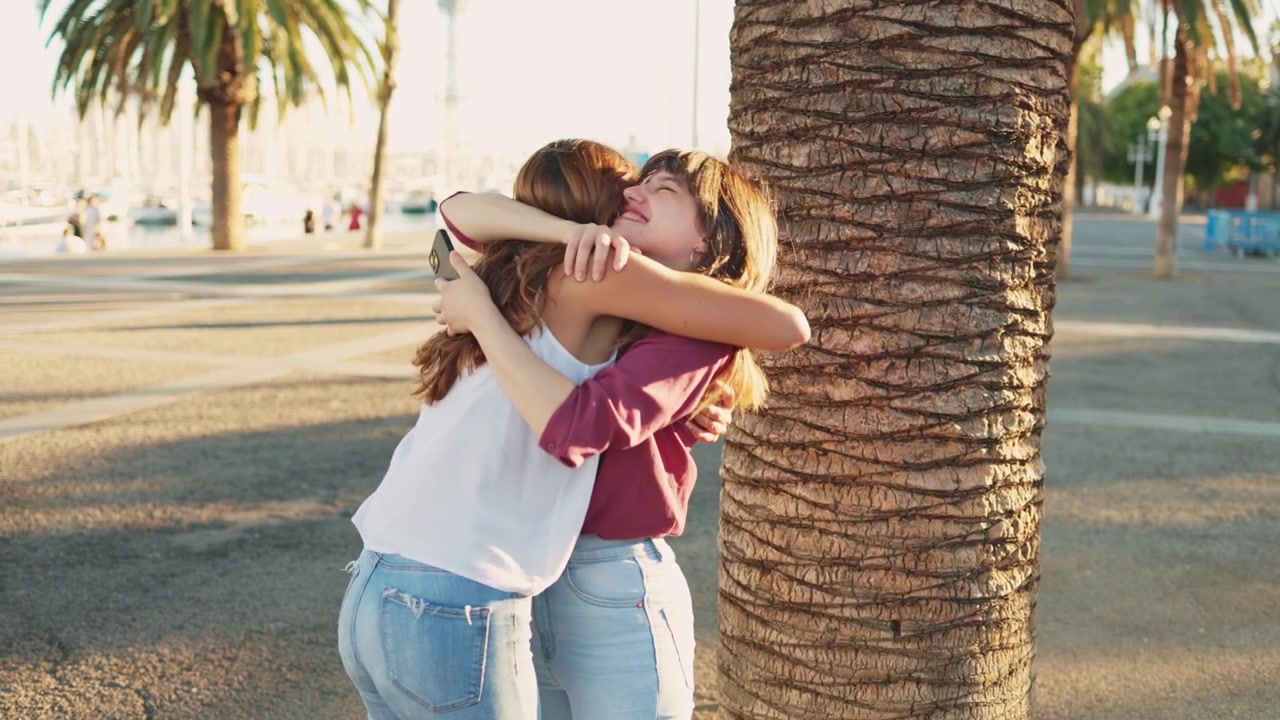 Felice ricongiungimento di due amiche che si abbracciano all'aperto vicino a una palma