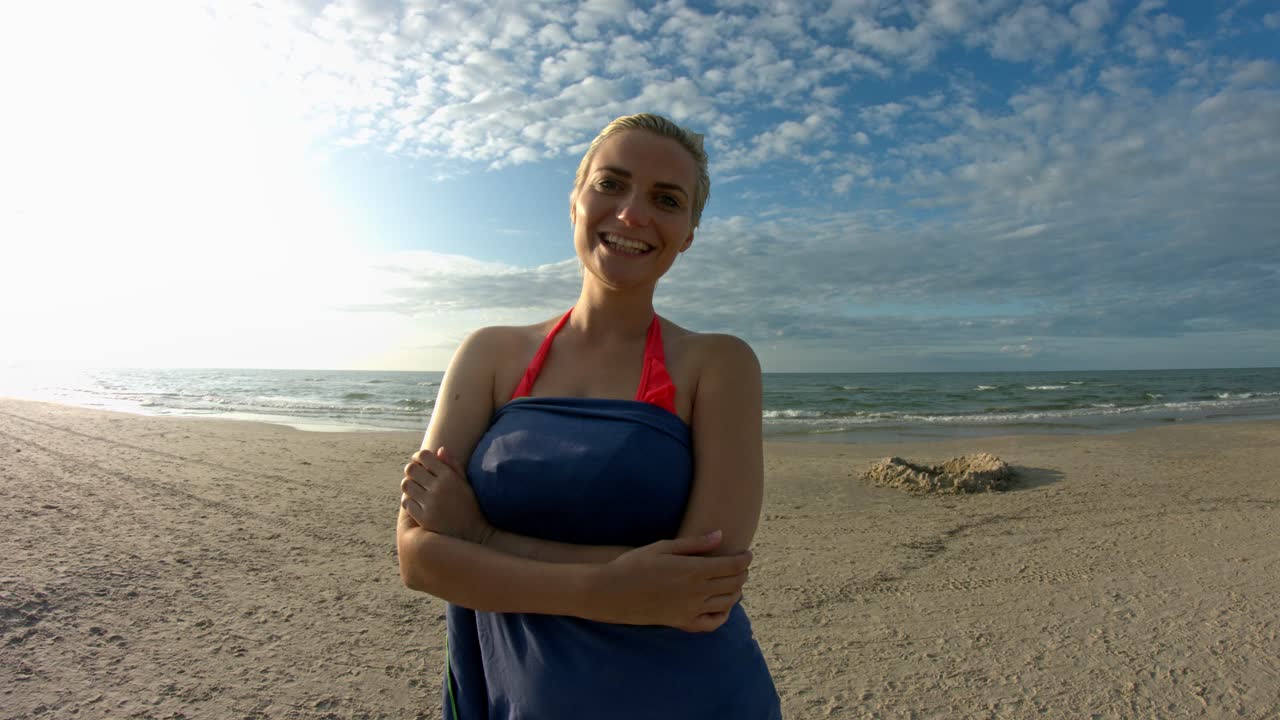 Een vrouw met kort blond haar droogt zich af na het zwemmen op het strand, glimlachend en lachend naar de camera