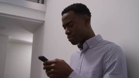 joven empresario en la oficina mirando el mensaje con malas noticias en el teléfono móvil y apoyado contra la pared mirando infeliz y deprimido disparado en tiempo real