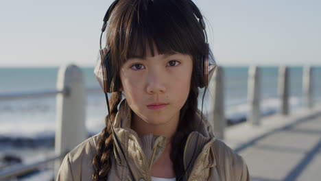 retrato de cerca de una hermosa niña asiática que se ve seria tranquila niño pequeño con auriculares escuchando música en una playa soleada en cámara lenta