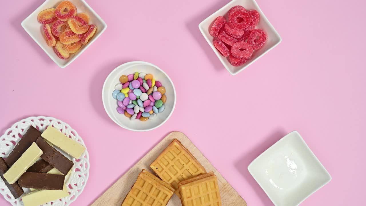 パステルピンクをテーマにボウルを満たす甘いキャンディ、ロリポップ、チョコレート。ストップモーションのフラットレイアニメーション。