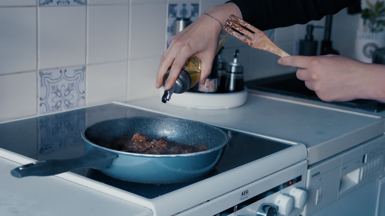 Kvinde tilbereder kød på en pande og tilsætter olivenolie og salt til saucen i et hvidt køkken om dagen i slowmotion.