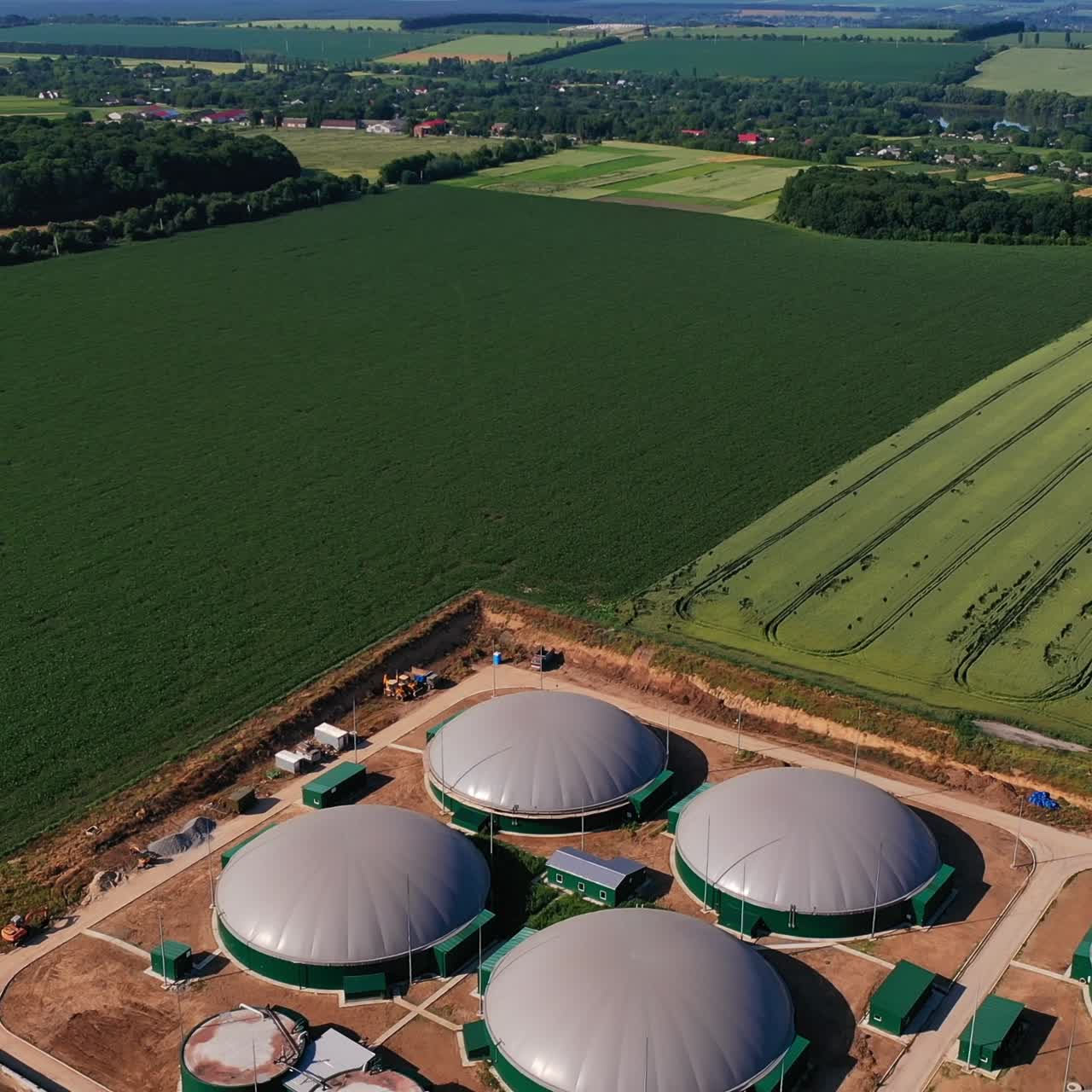 Plant for producing biofuel from biomass. A part of plant in the fields from air perspective. Farmlands, forests and villages at the backdrop