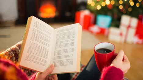 animation of hands of caucasian woman with coffee reading book at christmas time