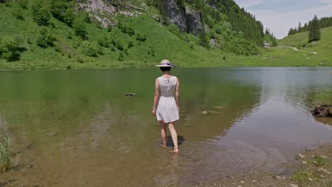 woman in white dress and hat stands by scenic talalpsee lake surrounded by lush green mountains