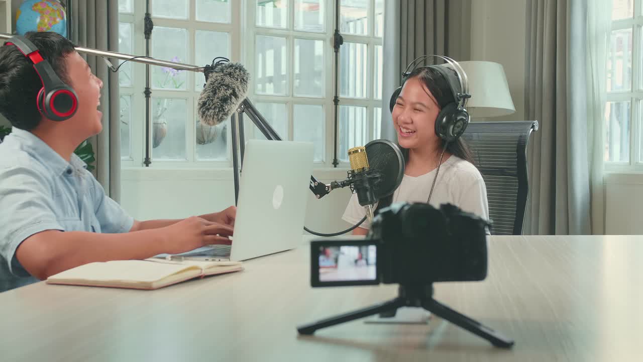 Camera Recording Of  Happy Asian Boy Host Record Podcast Use Microphone Wear Headphone With Laptop Interview Guest Conversation For Content In His Home Studio. Content Creator Concept