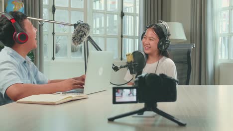 camera recording of  happy asian boy host record podcast use microphone wear headphone with laptop interview guest conversation for content in his home studio. content creator concept