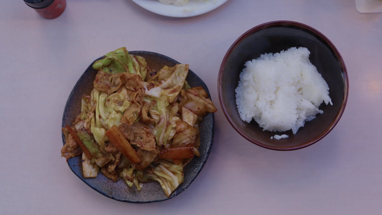 Mãos pousam prato de porco salteado com repolho e tigela de arroz no Japão
