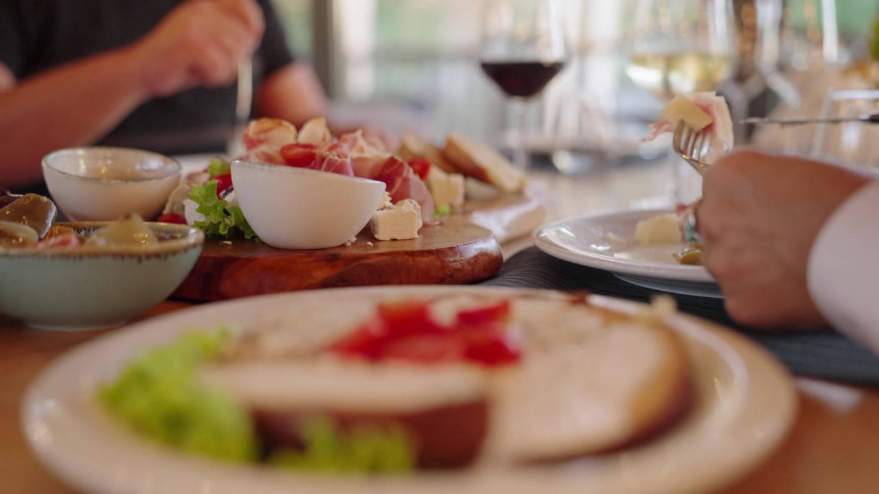 Persone che gustano un pasto condiviso e vino a un tavolo di un ristorante elegante in una calda luce diurna, un coltello che taglia il cibo.