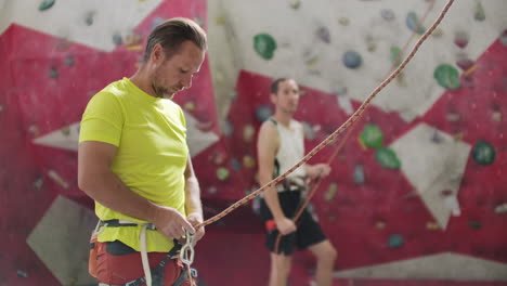 Close-up-of-Climber-man-belaying-another-climber-against-a-wall-with-hooks-in-slow-motion