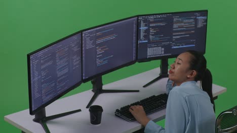 side view of bored asian woman developer write code with multiple computer screens in green screen studio