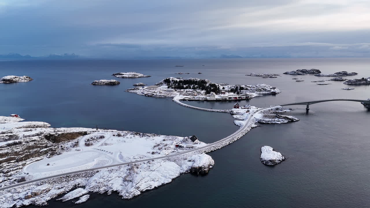 Cinematic aerial view of snowy coastal village and bridge in Lofoten, Norway, scenic arctic seascape with islands, winter shoreline, and dramatic Nordic landscape