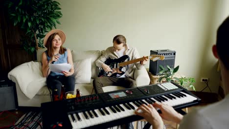 group of friends guitarist, singer and keyboarder are playing musical instruments and singing during band practice in home studio. music, friendship and people concept.