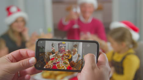 pov shot of person taking photo of multi-generation family meal at christmas on mobile phone